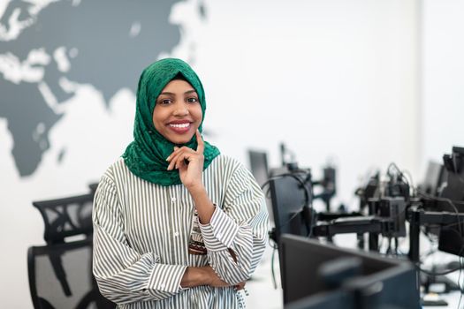 Portrait of Muslim black female software developer with green hijab standing at modern open plan startup office. Selective focus. High-quality photo