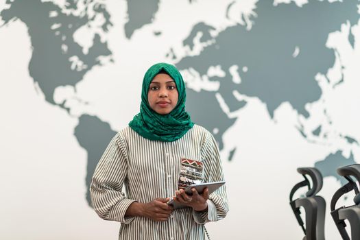 Portrait of Muslim female software developer with green hijab holding tablet computer while standing at modern open plan startup office. High-quality photo