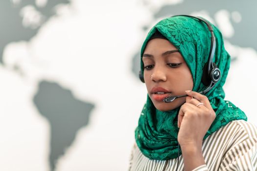 Afro Muslim female with green hijab scarf customer representative businesswoman with phone headset helping and supporting online with the customer in a modern call center. High-quality photo