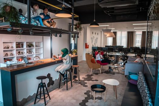 Group of casual multiethnic businesspeople taking a break from the work doing different things while enjoying free time in relaxation area at modern open plan startup office. High-quality photo