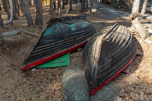 Two old fishing boats lie on the shore of the mountain lake pier in the forest. Overturned wooden boats on the coastal strip or coast. Shoreline