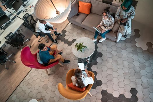 Top view photo of Multiethnic startup business team having brainstorming in relaxation area of modern office interior working on laptop and tablet computer. High-quality photo