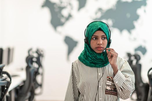 Afro Muslim female with green hijab scarf customer representative businesswoman with phone headset helping and supporting online with the customer in a modern call center. High-quality photo