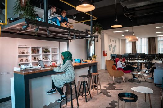 Group of casual multiethnic businesspeople taking a break from the work doing different things while enjoying free time in relaxation area at modern open plan startup office. High-quality photo