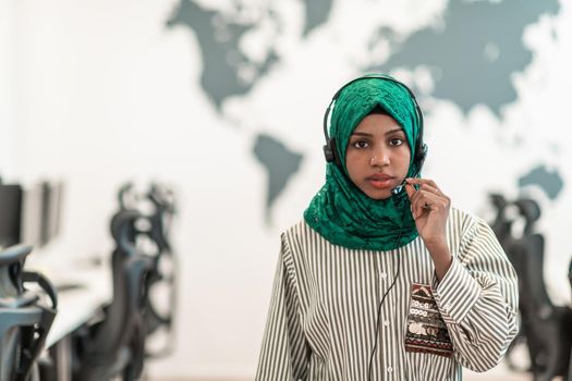 Afro Muslim female with green hijab scarf customer representative businesswoman with phone headset helping and supporting online with the customer in a modern call center. High-quality photo