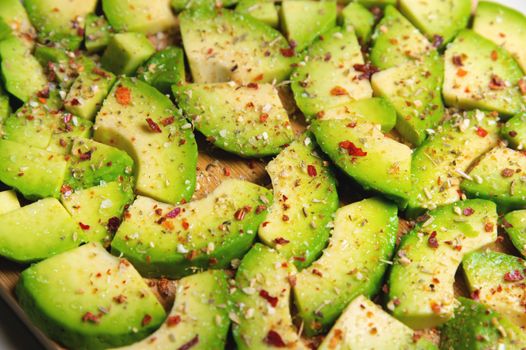 Large slices of sliced ripe avocado lie textured on a wooden cutting board. Sprinkled with spices. Healthy food. Vegetarianism.
