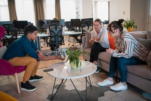 Multiethnic startup business team having brainstorming in relaxation area of modern office interior working on laptop and tablet computer. High-quality photo