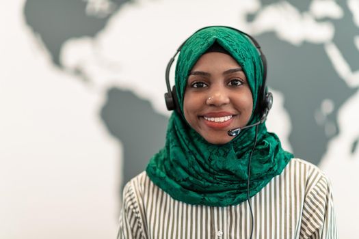 Afro Muslim female with green hijab scarf customer representative businesswoman with phone headset helping and supporting online with the customer in a modern call center. High-quality photo