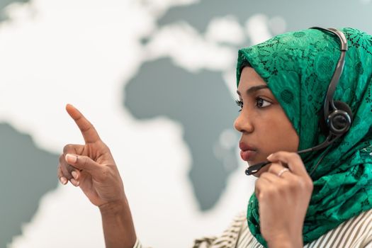 Afro Muslim female with green hijab scarf customer representative businesswoman with phone headset helping and supporting online with the customer in a modern call center. High-quality photo