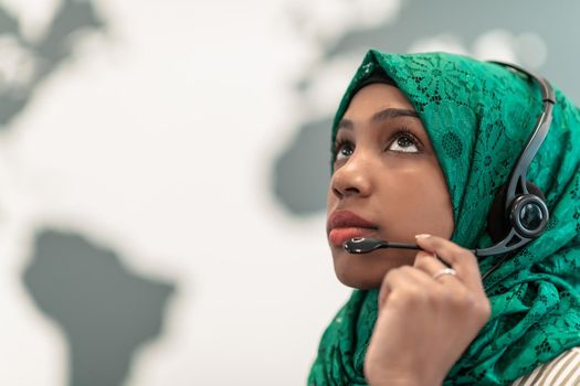 Afro Muslim female with green hijab scarf customer representative businesswoman with phone headset helping and supporting online with the customer in a modern call center. High-quality photo