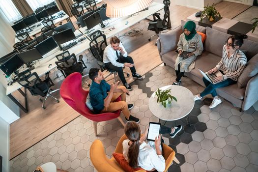 Top view photo of Multiethnic startup business team having brainstorming in relaxation area of modern office interior working on laptop and tablet computer. High-quality photo