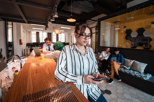 Businesswoman with glasses using a smartphone at modern startup open plan office interior. Selective focus. High-quality photo