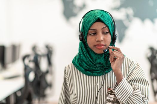 Afro Muslim female with green hijab scarf customer representative businesswoman with phone headset helping and supporting online with the customer in a modern call center. High-quality photo