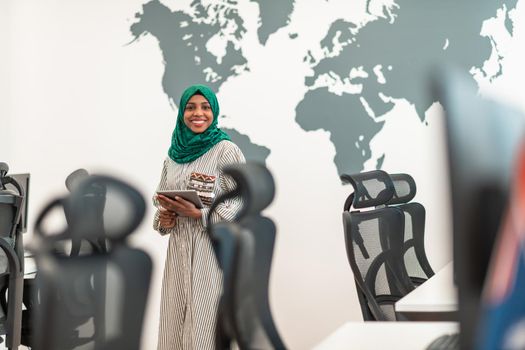 Portrait of Muslim female software developer with green hijab holding tablet computer while standing at modern open plan startup office. High-quality photo