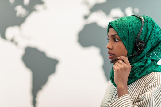 Afro Muslim female with green hijab scarf customer representative businesswoman with phone headset helping and supporting online with the customer in a modern call center. High-quality photo