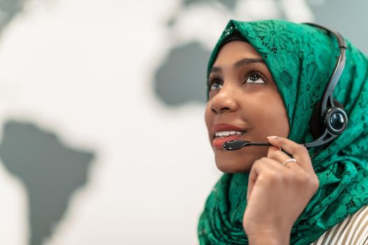 Afro Muslim female with green hijab scarf customer representative businesswoman with phone headset helping and supporting online with the customer in a modern call center. High-quality photo