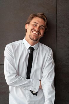 Portrait of startup businessman in a white shirt with a black tie standing in front of the gray wall outside. High-quality photo