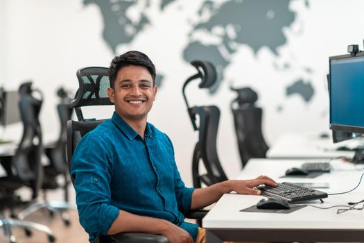 Casual businessman working on a desktop computer in modern open plan startup office interior. Selective focus. High-quality photo