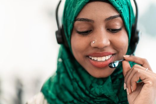 Afro Muslim female with green hijab scarf customer representative businesswoman with phone headset helping and supporting online with the customer in a modern call center. High-quality photo