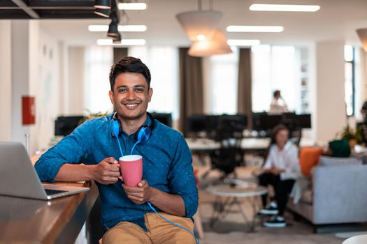 Casual businessman taking a break from the work using a laptop while drinking tea in relaxation area of modern open plan startup office. High-quality photo