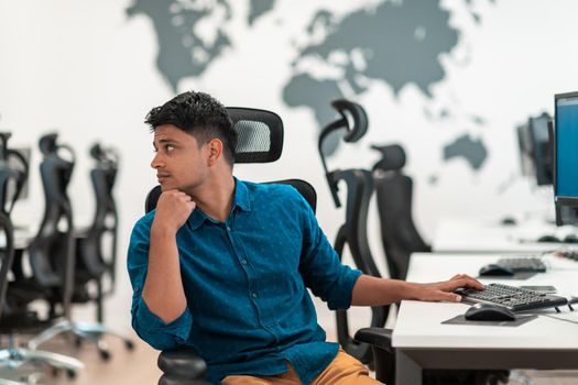 Casual businessman working on a desktop computer in modern open plan startup office interior. Selective focus. High-quality photo