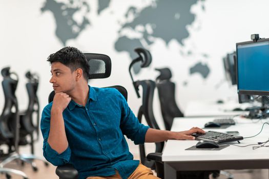 Casual businessman working on a desktop computer in modern open plan startup office interior. Selective focus. High-quality photo