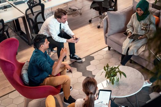 Multiethnic startup business team having brainstorming in relaxation area of modern office interior working on laptop and tablet computer. High-quality photo