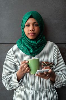 African Muslim businesswoman with green hijab using a smartphone during a coffee break from work outside. High-quality photo