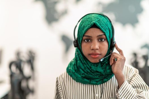 Afro Muslim female with green hijab scarf customer representative businesswoman with phone headset helping and supporting online with the customer in a modern call center. High-quality photo