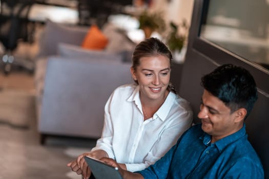 Multiethnic business people man with a female colleague working together on tablet computer in relaxation area of modern startup office. High-quality photo