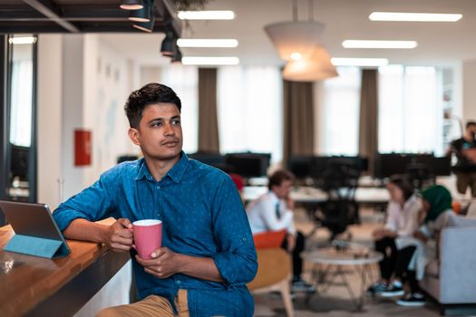 Casual businessman taking a break from the work using a laptop while drinking tea in relaxation area of modern open plan startup office. High-quality photo