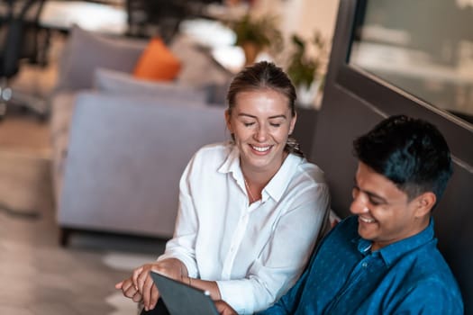 Multiethnic business people man with a female colleague working together on tablet computer in relaxation area of modern startup office. High-quality photo