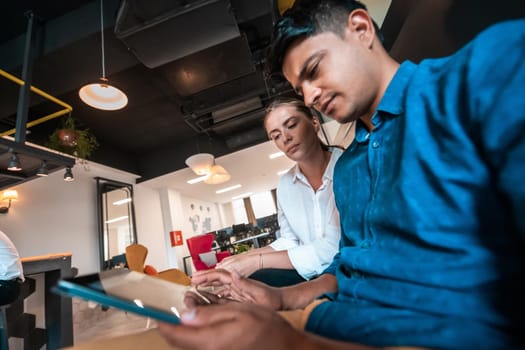 Multiethnic business people man with a female colleague working together on tablet computer in relaxation area of modern startup office. High-quality photo