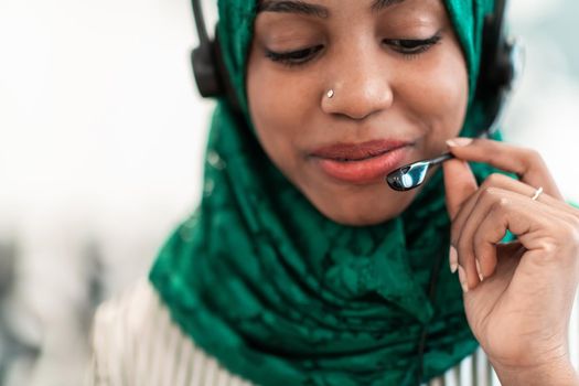 Afro Muslim female with green hijab scarf customer representative businesswoman with phone headset helping and supporting online with the customer in a modern call center. High-quality photo