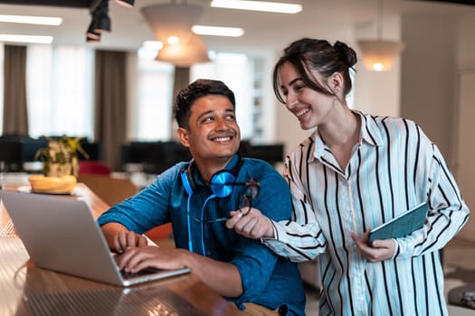 Multiethnic business people man with a female colleague working together on tablet and laptop computer in relaxation area of modern startup office. High-quality photo