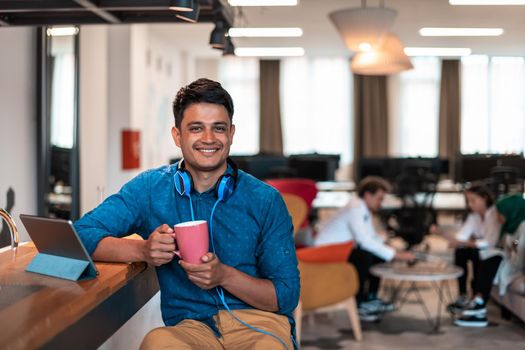 Casual businessman taking a break from the work using a laptop while drinking tea in relaxation area of modern open plan startup office. High-quality photo