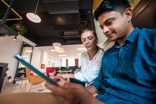 Multiethnic business people man with a female colleague working together on tablet computer in relaxation area of modern startup office. High-quality photo