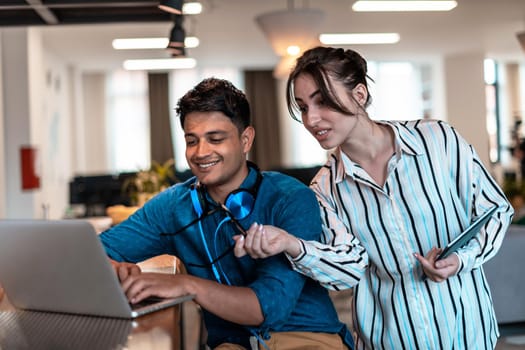 Multiethnic business people man with a female colleague working together on tablet and laptop computer in relaxation area of modern startup office. High-quality photo