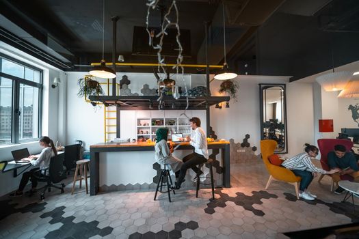 Group of casual multiethnic businesspeople taking a break from the work doing different things while enjoying free time in relaxation area at modern open plan startup office. High-quality photo