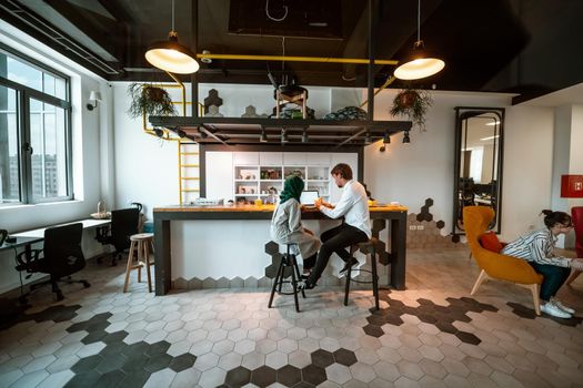 Group of casual multiethnic businesspeople taking a break from the work doing different things while enjoying free time in relaxation area at modern open plan startup office. High-quality photo