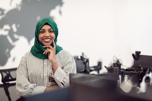 Portrait of Muslim black female software developer with green hijab standing at modern open plan startup office. Selective focus. High-quality photo