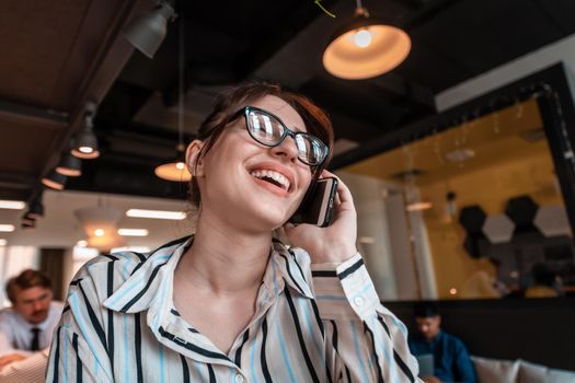 Businesswoman with glasses using a smartphone at modern startup open plan office interior. Selective focus. High-quality photo