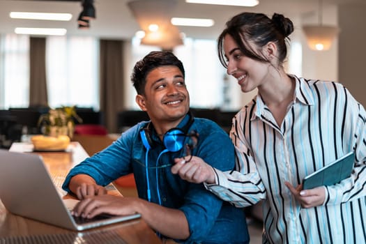 Multiethnic business people man with a female colleague working together on tablet and laptop computer in relaxation area of modern startup office. High-quality photo