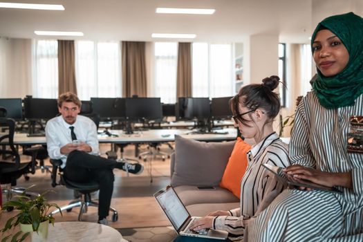 Multiethnic startup business team having brainstorming in relaxation area of modern office interior working on laptop and tablet computer. High-quality photo