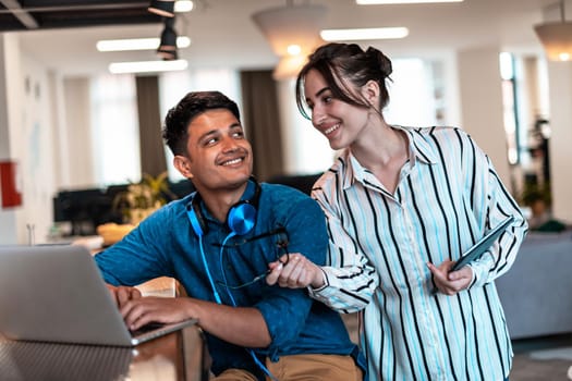 Multiethnic business people man with a female colleague working together on tablet and laptop computer in relaxation area of modern startup office. High-quality photo