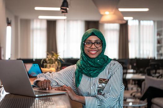 Businesswoman wearing a green hijab using laptop in relaxation area at modern open plan startup office. Selective focus. High-quality photo