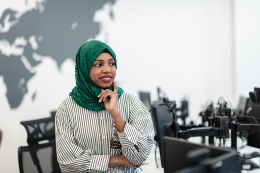 Portrait of Muslim black female software developer with green hijab standing at modern open plan startup office. Selective focus. High-quality photo