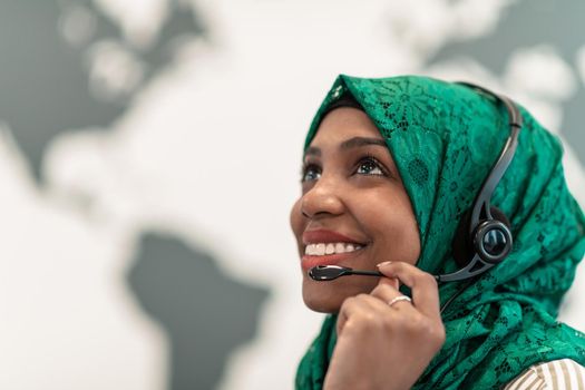 Afro Muslim female with green hijab scarf customer representative businesswoman with phone headset helping and supporting online with the customer in a modern call center. High-quality photo