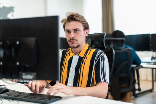 Casual man working on a desktop computer in modern open plan startup office interior. Selective focus. High-quality photo