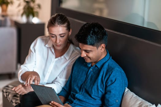 Multiethnic business people man with a female colleague working together on tablet computer in relaxation area of modern startup office. High-quality photo